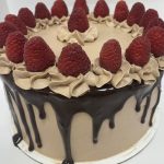 image of a cake with brown frosting, chocolate drip and raspberries around the top edge